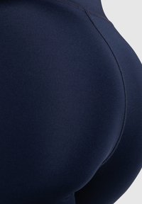 Leggings sportivi blu navy con un design aderente, caratterizzati da una texture liscia e dettagli di cucitura, che evidenziano l'elasticità del tessuto e la sua capacità di mantenere la forma.