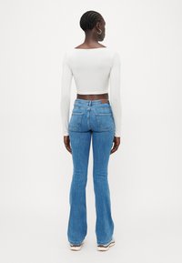 Blå utsvängda jeans med hög midja och en kortärmad vit topp. Har fickor och en figurnära silhuett. Slät textur.