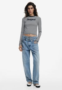 Pruhovaná blúzka s dlhým rukávom s kratším strihom, skombinovaná s voľnými svetlomodrými denimovými džínsami s vreckami a vysokým pásom. Čierno-biela obuv.