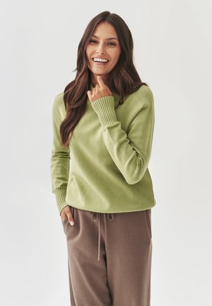Light green knitted sweater with ribbed cuffs and neckline, paired with brown jogger pants. Smooth texture and relaxed fit.