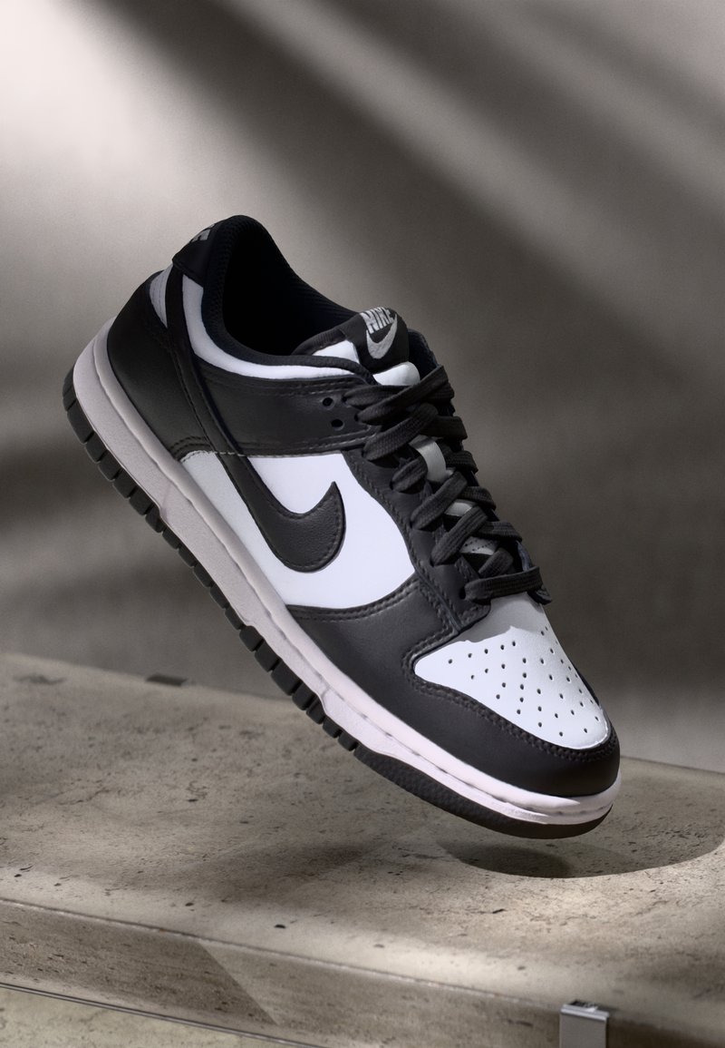 Melnbaltas Nike Dunk Low sporta apavi ar ādas augšdaļu, caurdurta pirkstu kaste un melnām šņorēm, ar baltu zoli un logo akcentiem.