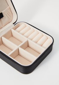 Black zippered jewelry case with beige soft lining, featuring several compartments and roll spaces for organized storage.