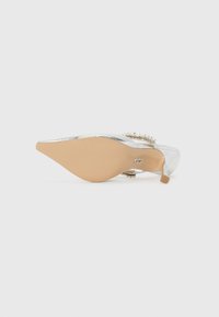 Silver high-heeled shoe with a pointed toe, adorned with a crystal accent along the strap, featuring a light brown sole and a glossy finish.