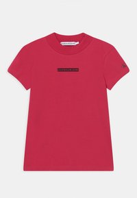 Czerwona bawełniana koszulka z krótkim rękawem, okrąg�łym dekoltem, z czarnym prostokątnym logo "CALVIN KLEIN JEANS" na piersi. Gładka faktura.