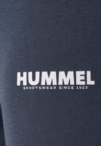Marinblått tyg med en slät yta som har en vit "HUMMEL"-logotyp och texten "SPORTSWEAR SINCE 1923" på den nedre sidan.