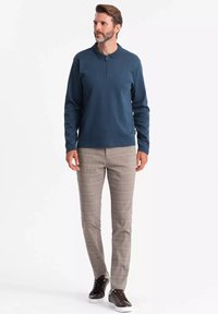 Langarm-Polo für Herren aus dunkelblauem Stoff, kombiniert mit hellgrauen karierten Hosen. Schwarze Sneakers runden das Outfit ab.