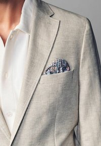 Lys beige linned blazer med klapkrave, parret med en hvid struktureret skjorte. Har en paisley lommefyr i blå, pink og grønne nuancer.