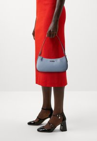 Jasnoniebieska torebka o fakturze z krótkim uchwytem, z srebrnymi akcentami i logo "HUGO". Noszona z czerwoną sukienką i czarnymi lakierowanymi szpilkami.