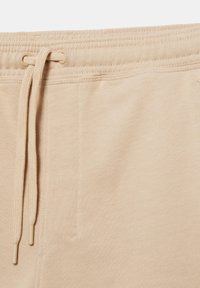 Ceinture de pantalon de survêtement beige avec bande élastique et cordon assorti noué à travers des œillets métalliques.