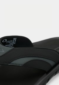 Sandalia negra con plantilla acolchada y correas texturizadas. Presenta un diseño redondeado y un logo en relieve en la correa. Talla 10.0.