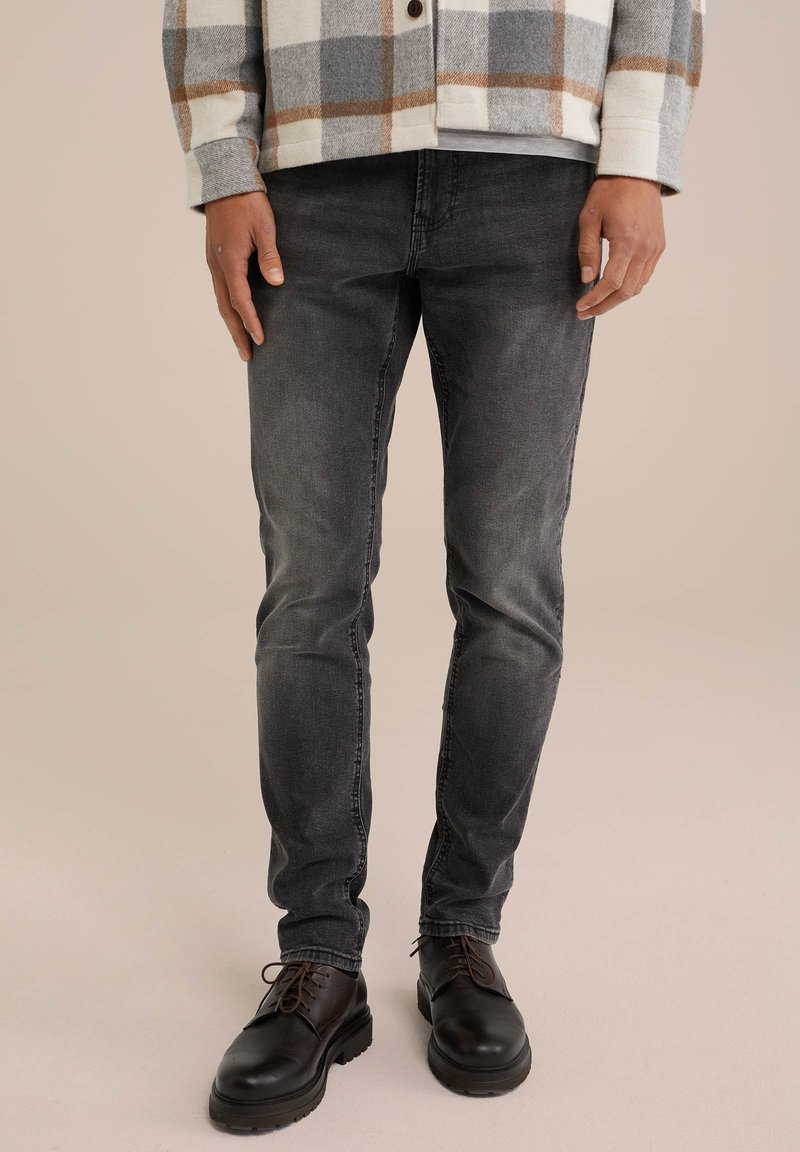 Jeans gris oscuro con corte ajustado, con un desvanecimiento sutil. Llevados con botas negras de cordones para un look casual.