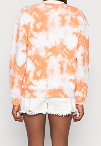 Oranžová a bílá mikina s technikou tie-dye s dlouhými rukávy a žebrovanými manžetami, doplněná o třepené bílé šortky. Měkká látka, pohodlný střih.