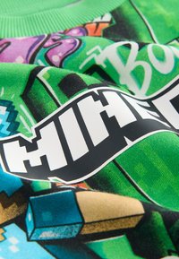 Groene grafische sweater met videospelbeelden, dikke zwarte letters en verschillende kleuren in het ontwerp, gemaakt van een zachte, gestructureerde stof.