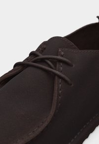 Σκούρο καφέ δερμάτινο casual παπούτσι με στρογγυλεμένη μύτη και δεμένα κορδόνια, απεικονίζεται με φόντο απλό ανοιχτό.