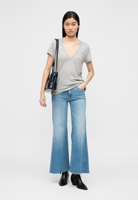 Gray v-neck t-shirt, light blue flared jeans with frayed hem, and black ankle boots. Model carries a small black handbag.