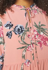 Vaaleanpunainen kukkakuosiset paita, jossa on pyöreä pääntie, avainreikäyksityiskohta ja kiristysnauha. Kangas on kevyttä ja pehmeää.