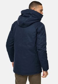 Marineblå, isoleret jakke med hætte, der har en glat tekstur og en lige silhuet. Udstyret med en skjult lynlås og sidelommer.