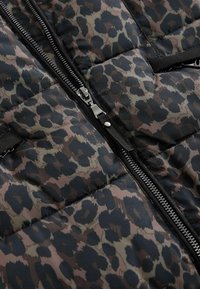 Béžová vesta s potlačou leopardieho vzoru, obsahujúca odtiene hnedej a čiernej farby, so zipsom vpredu a dvoma bočnými vreckami.