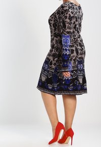 Robe en mélange de laine avec un motif floral et chouette en bleu et gris, dotée d'une jupe évasée. Complétée par des chaussures à talons hauts rouges.