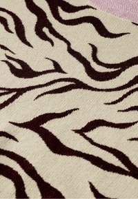 Tissu tricoté avec une base beige et un motif de rayures irrégulières de tigre brun foncé, comportant une petite section incurvée rose en haut du bord.