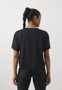 Svart t-skjorte med korte ermer laget av glatt stoff, med en løs passform og rund hals, brukt sammen med svarte leggings.