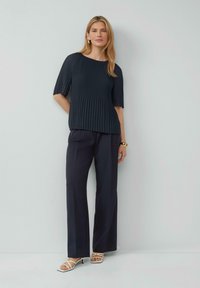 Haut plissé marine à manches courtes associé à un pantalon large marine et des sandales blanches à lanières. Texture lisse et coupe décontractée.