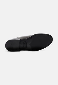 Scarpa di pelle con una finitura nera lucida, punta arrotondata e suola in gomma nera testurizzata. Presenta cuciture visibili e un marchio sulla suola.