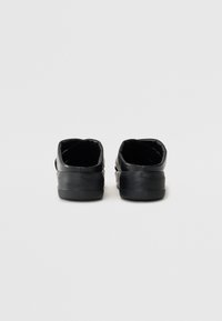 Schwarze Slipper aus glattem Leder, mit abgerundeter Form und strukturiertem Gummisohle, die eine geprägte Markenkennzeichnung an der Ferse aufweisen.