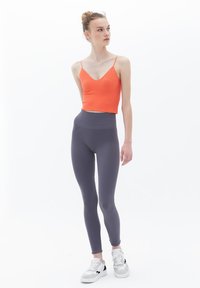 Top a coste arancione con spalline sottili, abbinato a leggings grigi lisci a vita alta. Il modello indossa sneakers bianche con dettagli neri.