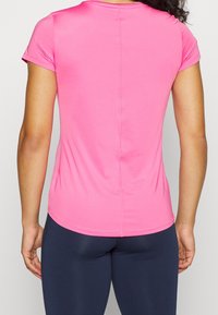 Top ajustado de manga corta en tejido rosa brillante, con un diseño sin costuras, cuello redondeado y una sutil costura vertical en la parte posterior.