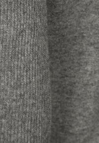 Tissu en maille grise avec une texture côtelée fine, présentant différentes nuances de gris, mettant en valeur des fibres douces et mélangées.