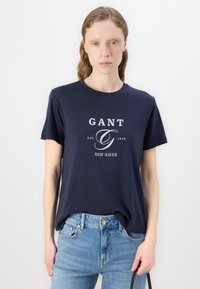 Marineblå kortærmet T-shirt med hvid "GANT" logo og teksten "EST. 1949 NEW HAVEN". Blødt bomuldsstof, løs pasform, rund halsudskæring.