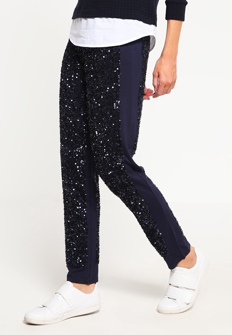 Marinblå glittriga träningsbyxor har en slim fit med slätt tyg på sidorna och glittrande dekor, kombinerat med vita sportskor.