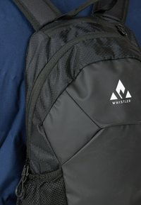 Black backpack featuring a textured fabric with a diamond pattern, adjustable shoulder straps, and a contrasting white logo on the side.