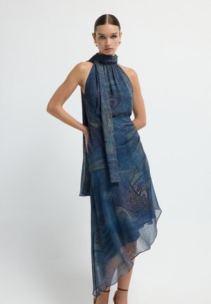 Robe halter asymétrique bleue, avec un motif paisley. Fabriquée en tissu léger avec un détail drapé et un voile transparent.
