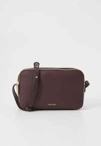 Geantă de umăr din piele bordeaux cu un fermoar aurit și un logo Calvin Klein pe față, având un bretele detașabil.
