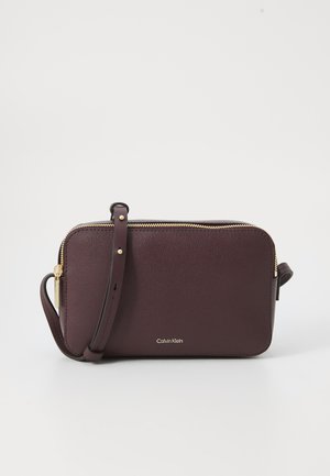 Borsa a tracolla in pelle borgogna con cerniera dorata e logo Calvin Klein sul davanti, dotata di una tracolla staccabile.