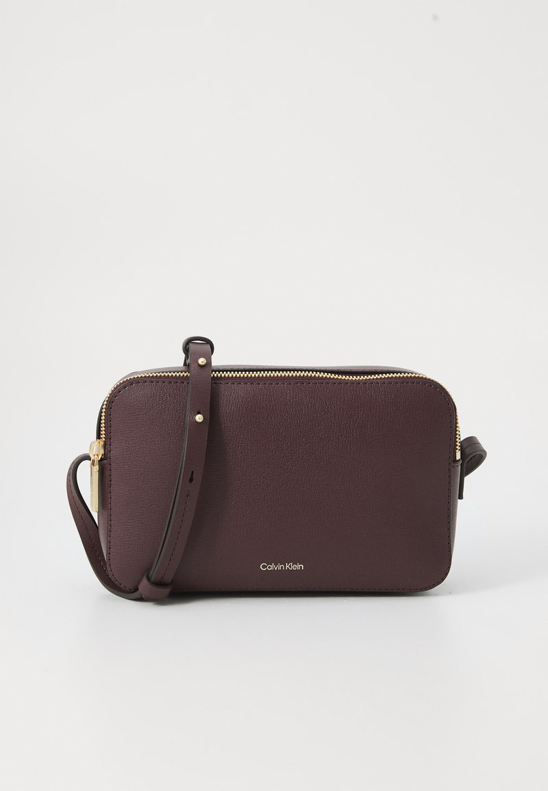Bolso cruzado de cuero burdeos con una cremallera dorada y un logo de Calvin Klein en la parte frontal, que incluye una correa desmontable.