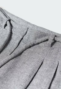 Tessuto grigio con un motivo a spina di pesce testurizzato, caratterizzato da pieghe e una vita. La vista ravvicinata enfatizza il materiale e i dettagli di design.