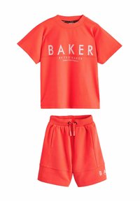 Punainen urheiluasu, johon kuuluu lyhythihainen t-paita, jossa on "BAKER" -logo, sekä yhteensopivat shortsit taskuilla ja joustavalla vyötäröllä.
