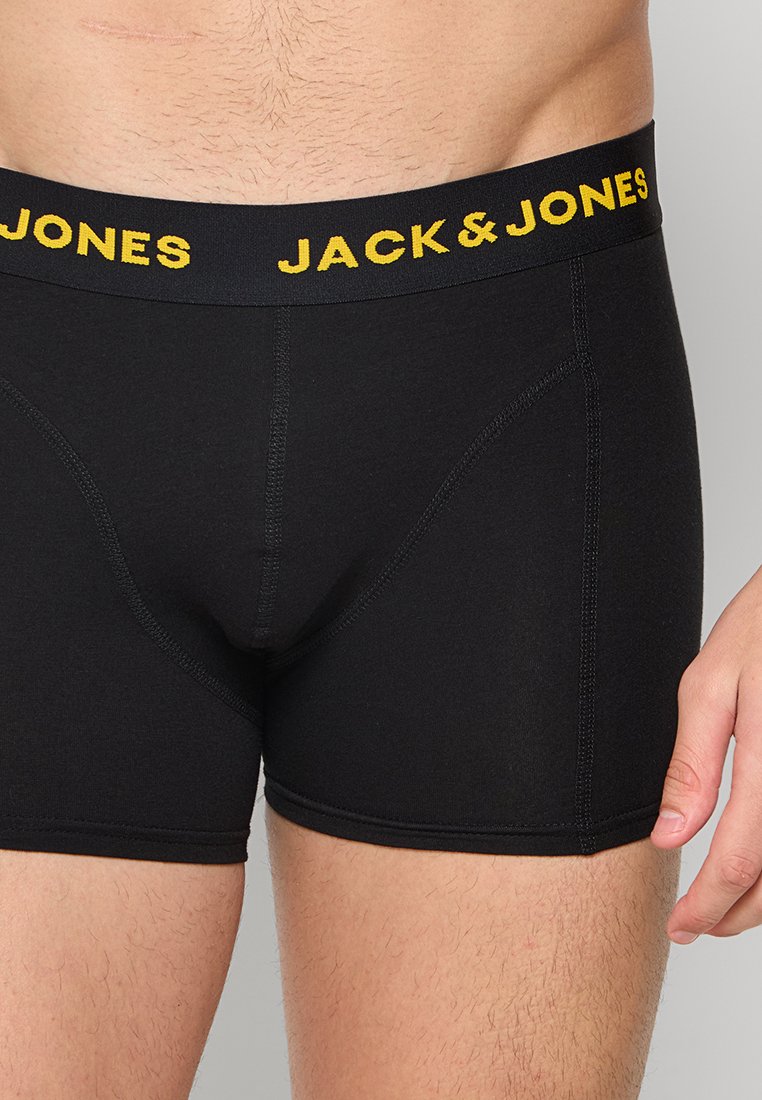 Cajas cortas negras hechas de tela elástica, con un logo amarillo "JACK & JONES" en la cinturilla y un diseño sin costuras para mayor comodidad.