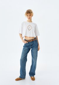 Hvid cropped t-shirt med diamantmønster, parret med løse blå denim jeans og brune snørebåndssko. Lige silhuet og afslappet design.