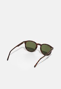 Gafas de sol redondas con un patrón de carey. Lentes verde oscuro, patillas delgadas con acentos metálicos, montura de plástico ligera.