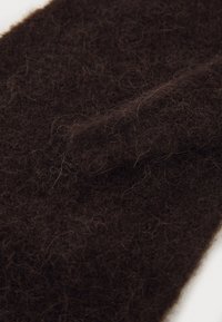 Tessuto di feltro marrone scuro con una consistenza morbida e pelosa, caratterizzato da fibre sciolte che creano un aspetto caldo e spesso.