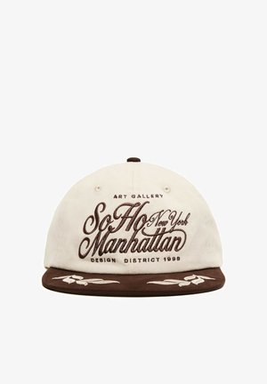 Casquette de baseball blanche et marron avec ""SoHo Manhattan New York"" brodé à l'avant et surpiqûres décoratives sur la visière marron.