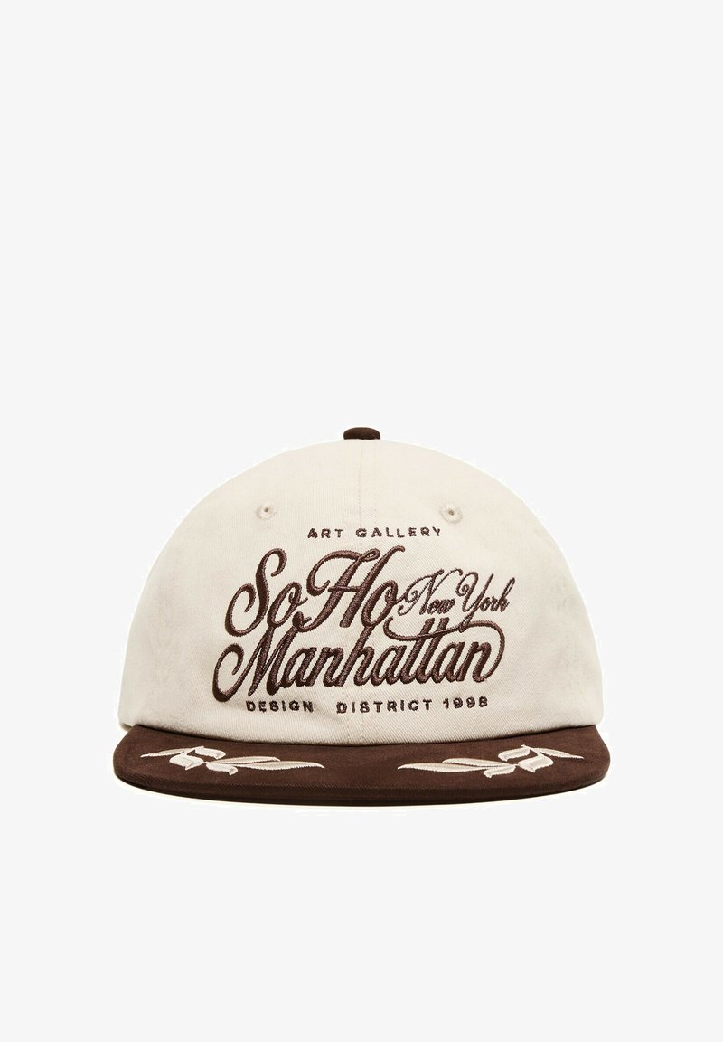 Casquette de baseball blanche et marron avec ""SoHo Manhattan New York"" brodé à l'avant et surpiqûres décoratives sur la visière marron.