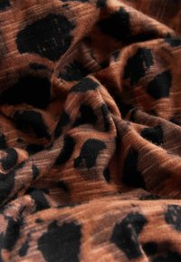 Látka s leopardím vzorem s měkkým, texturovaným povrchem. Dominantně oranžovo-hnědá s černými skvrnami, s mírně zvrásněným vzhledem.
