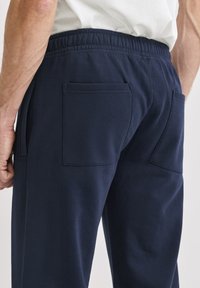 Laivastonsiniset puuvillaiset jogger-housut, joissa on joustava vyötärönauha, kaksi takataskua ja pehmeä, sileä pinta.