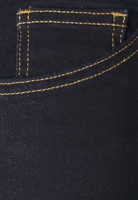 Mörk denimtyg med en framficka med guldstickning, slät textur och en klassisk femfickorsdesign.