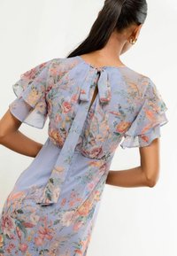 Abito floreale azzurro chiaro con maniche a volant, caratterizzato da una chiusura a occhiello sul retro con fiocco e diversi motivi floreali in colori pastello.